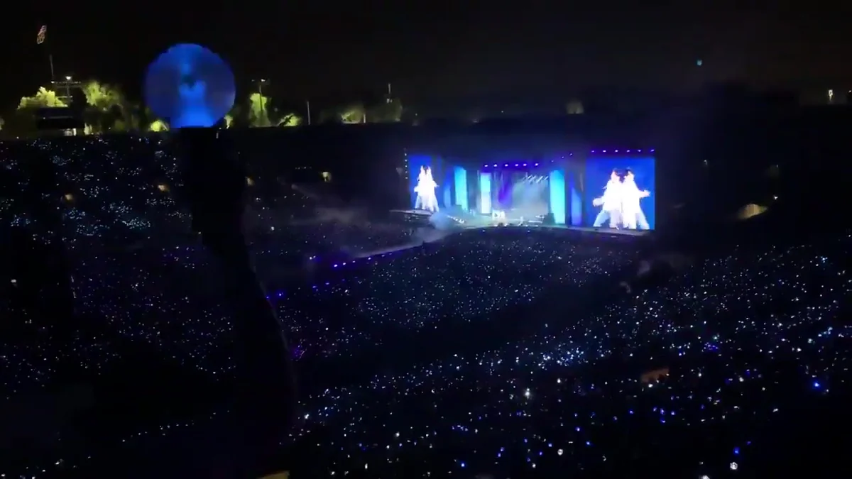 Crowd with blue lights and a stage in the distance during a BTS concert