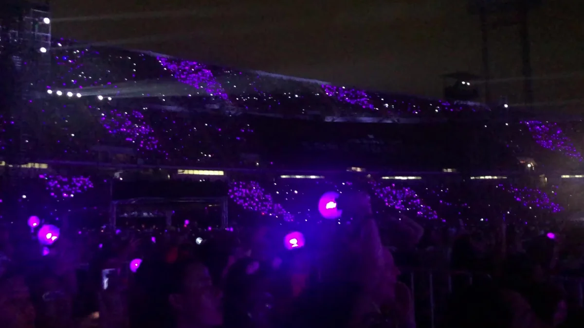 Stadium audience illuminated by purple lights, with light sticks raised in the foreground