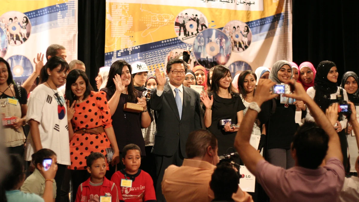 Grupo de participantes posa no palco enquanto pessoas na plateia tiram fotos.