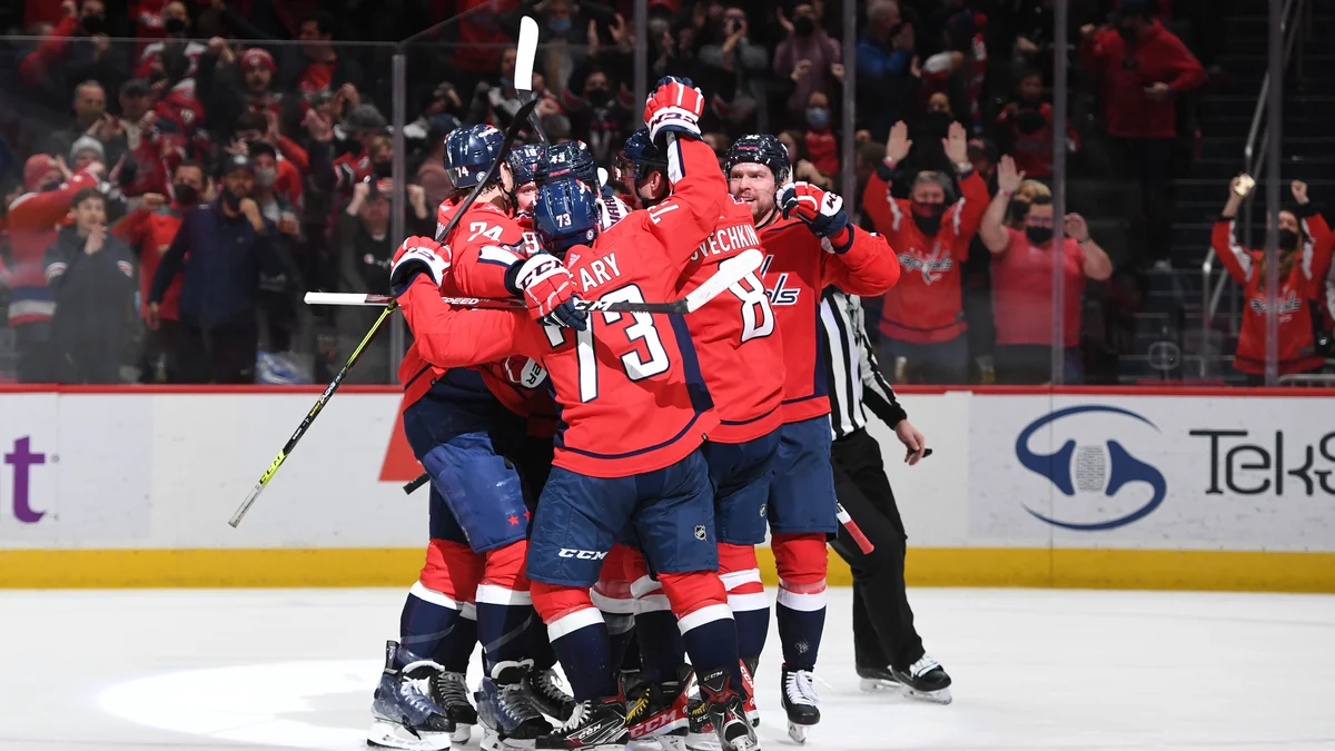 Jogadores do Washington Capitals com camisas vermelhas se abraçam no gelo diante da torcida.