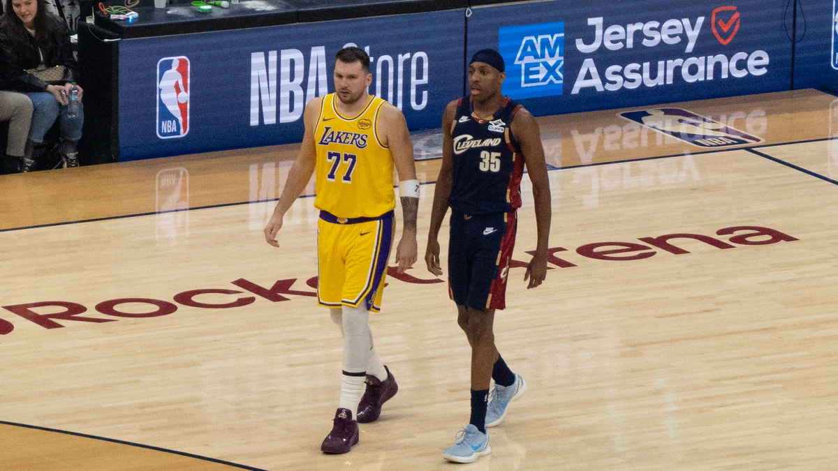 Luka Dončić camina por la cancha con el uniforme amarillo de los Lakers junto a Nae’Qwan Tomlin, de los Cavaliers.