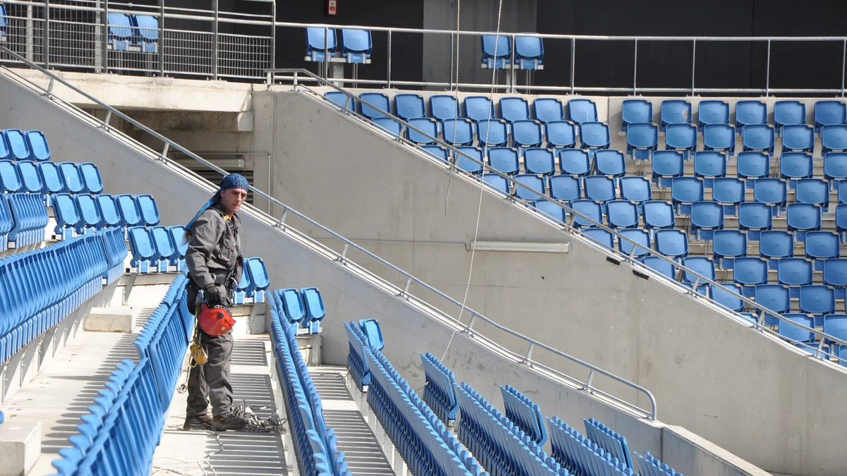 Worker in an aisle between rows of blue stadium seats