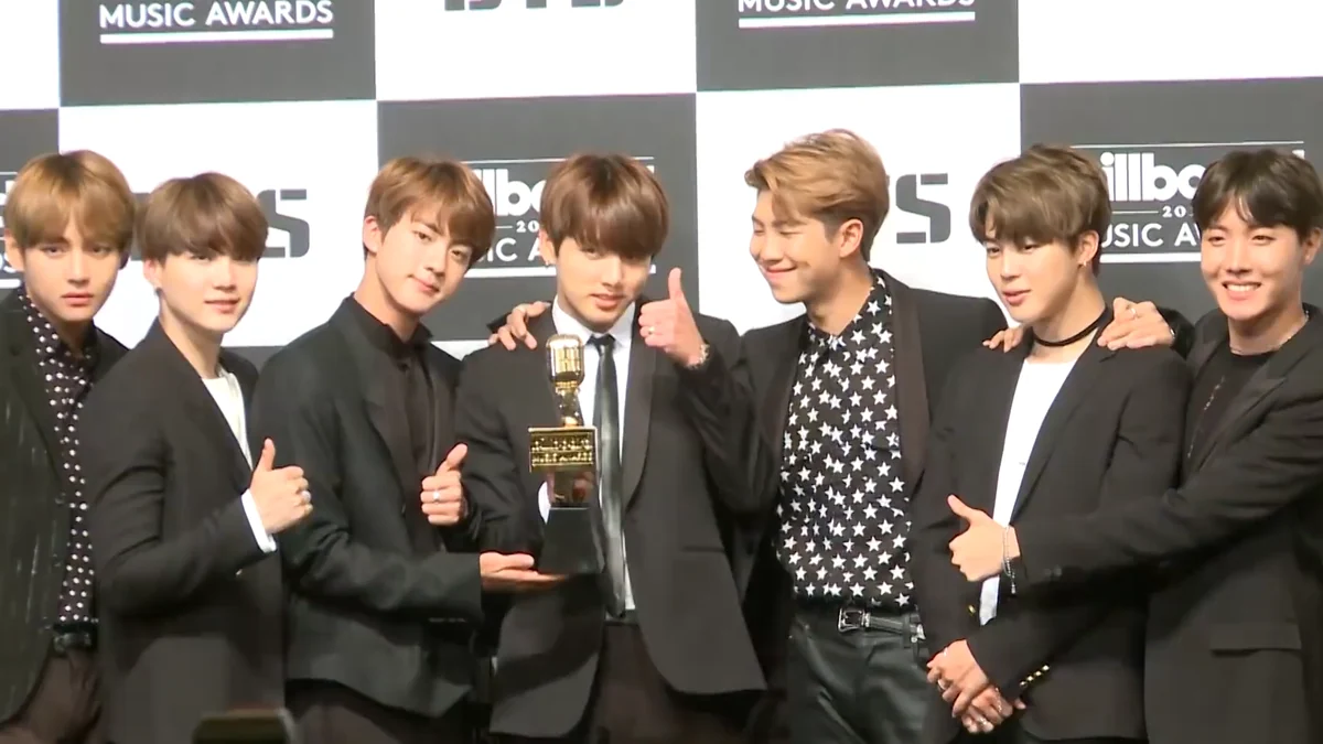 Los integrantes de BTS reunidos alrededor de un trofeo dorado ante un panel de prensa