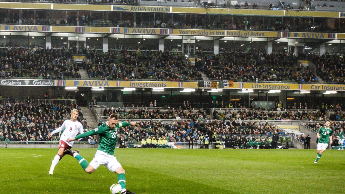 Jugador de verde patea el balón ante un rival de blanco en un estadio lleno.