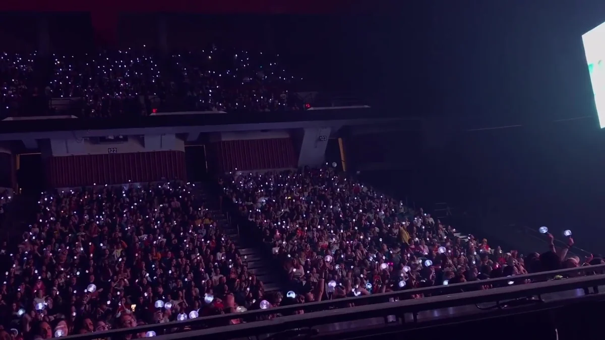 Arquibancadas de arena lotadas com fãs segurando luzes durante um show