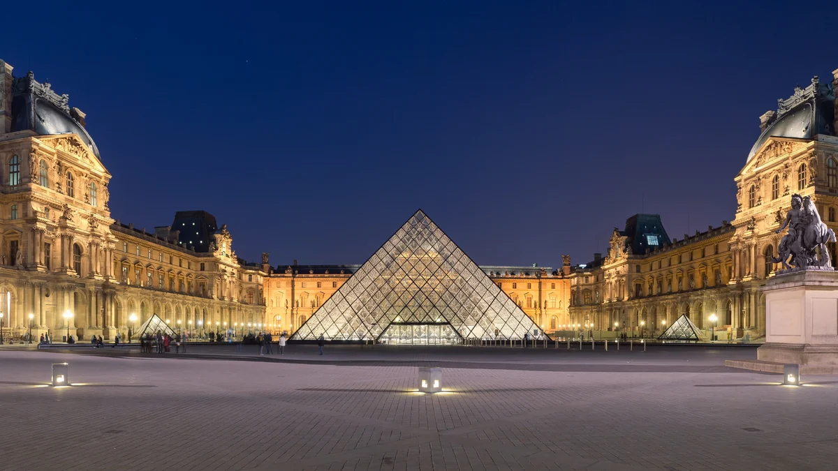 Pirâmide de vidro e fachadas iluminadas do Louvre à noite