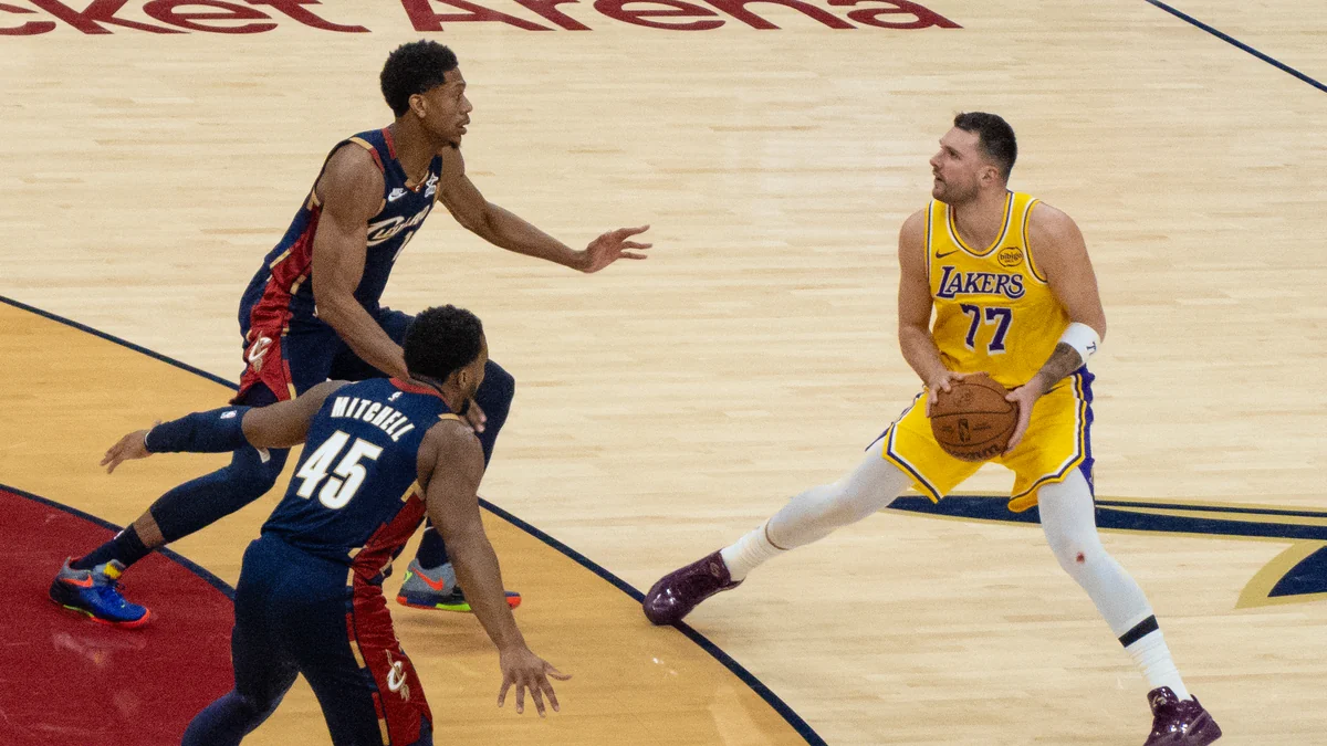 Luka Dončić segura a bola com o uniforme amarelo dos Lakers diante de dois defensores dos Cavaliers