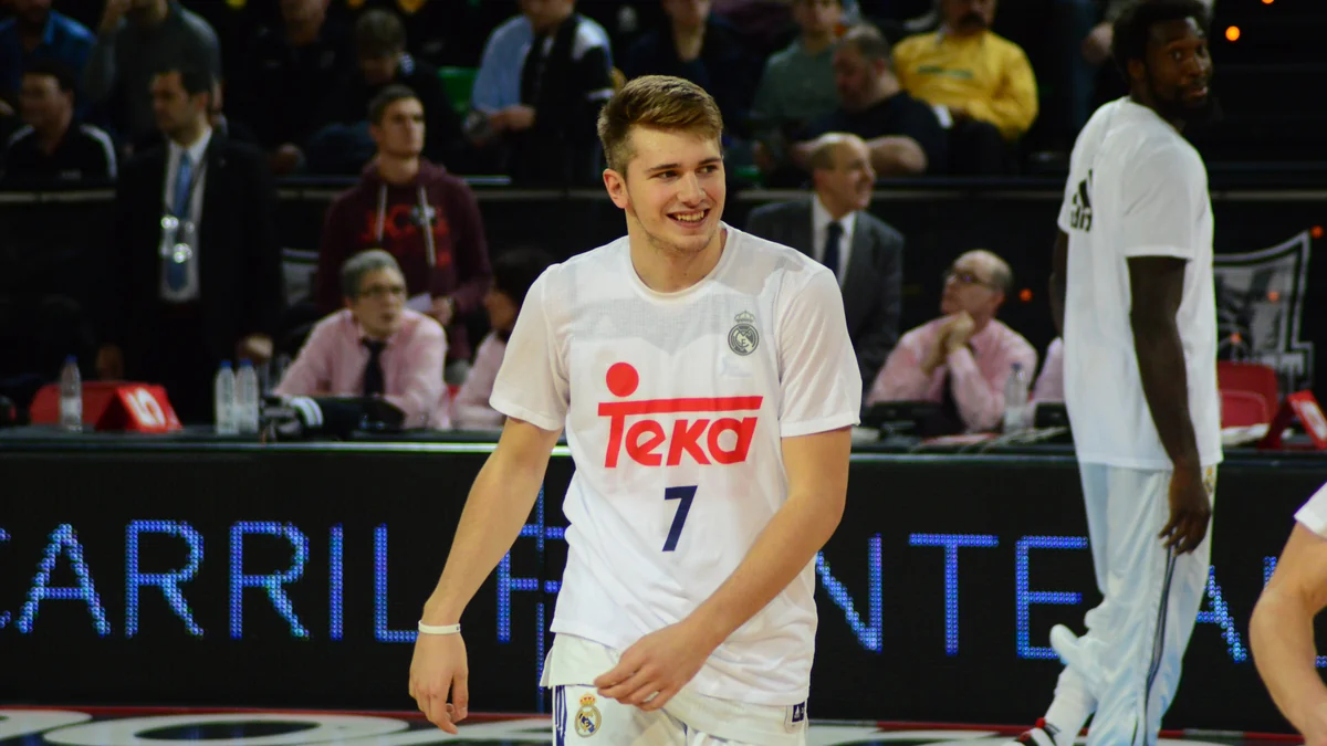Luka Dončić sorri em uma quadra usando camisa branca do Real Madrid com o número 7