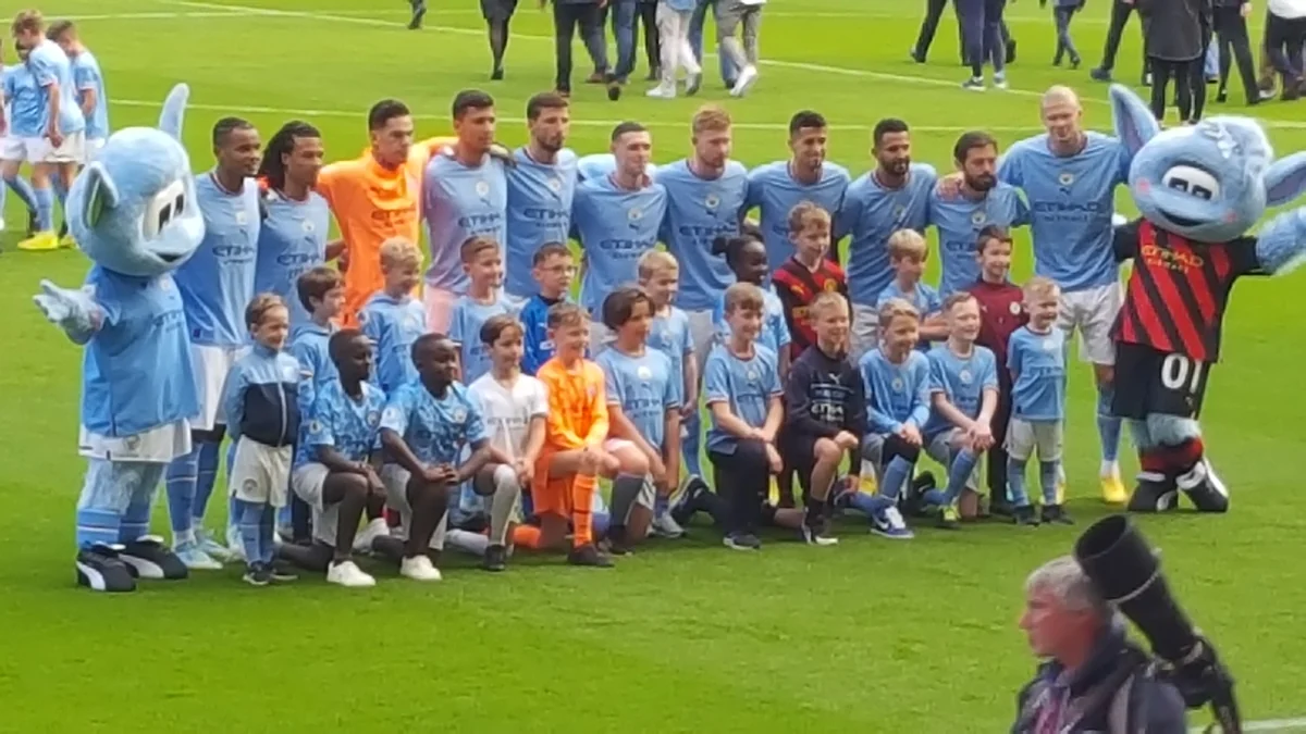 Manchester City players pose on the pitch with children and two club mascots