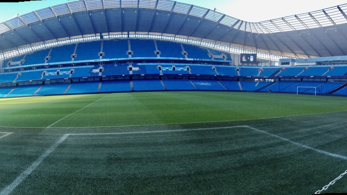 Césped visto de cerca y gradas azules vacías en el Etihad Stadium
