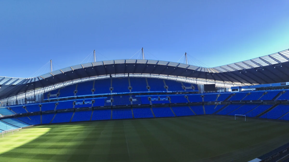 Gradas azules y césped del Etihad Stadium bajo un cielo despejado