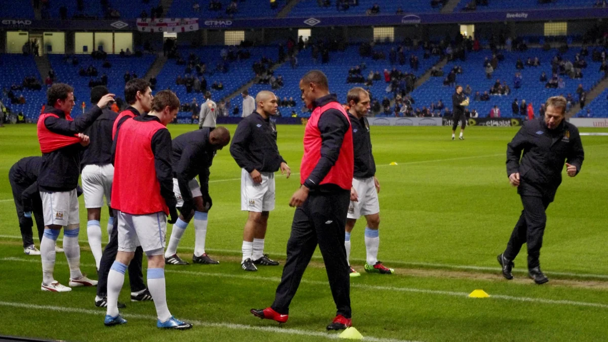 Jugadores del Manchester City calientan sobre el césped, algunos con petos rojos