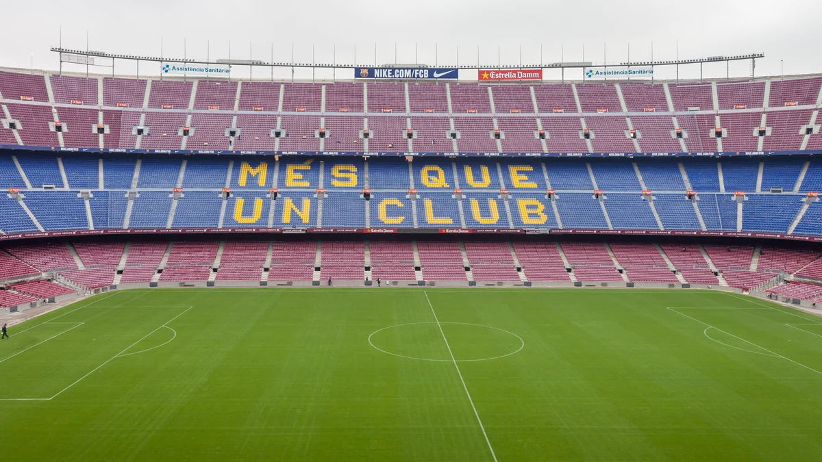 Empty interior of Camp Nou, with the pitch in the foreground and blue and maroon stands displaying the phrase “Més que un club”.