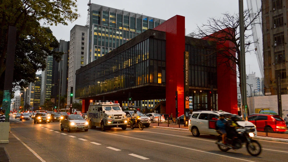 Vista lateral do MASP ao entardecer, com carros e motocicletas na Avenida Paulista