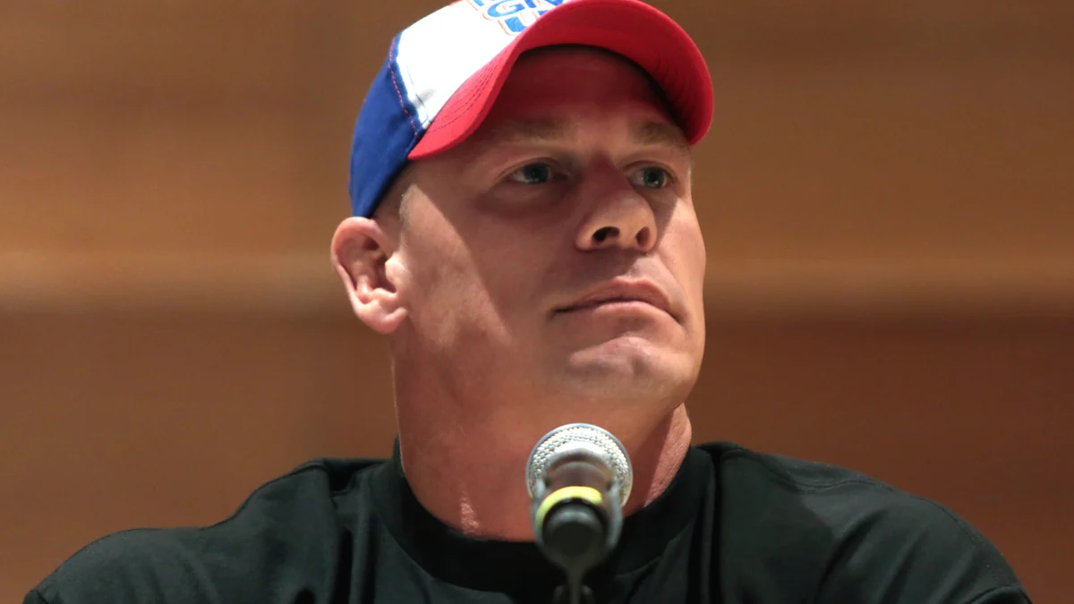John Cena con gorra ante un micrófono durante una mesa.