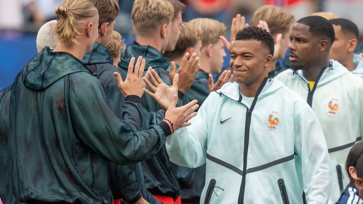 Kylian Mbappé cumprimenta jogadores alinhados antes de uma partida de futebol.