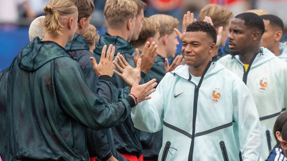 Kylian Mbappé cumprimenta jogadores alinhados antes de uma partida de futebol.
