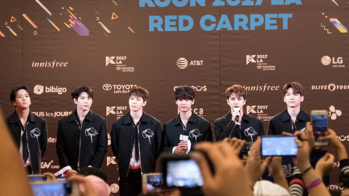 Six membres de VIXX devant le panneau du tapis rouge de KCON 2017 à Los Angeles, avec des appareils du public au premier plan