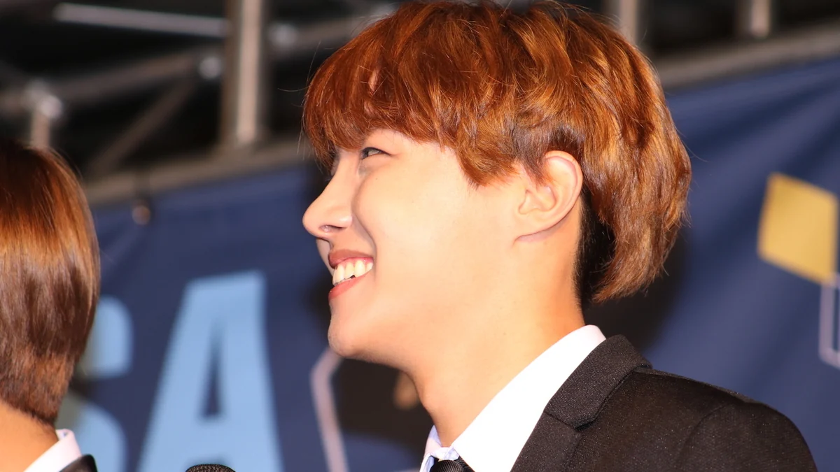 J-Hope souriant de profil en costume noir devant un fond bleu