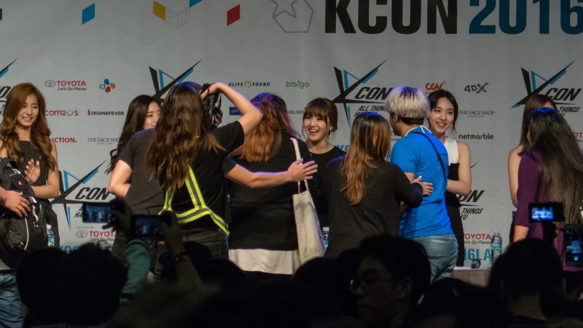 Des membres de Twice accueillent des fans devant un panneau de KCON 2016 à Los Angeles
