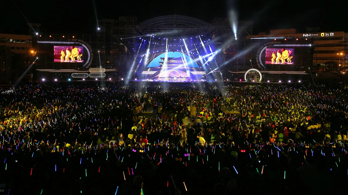 Gran público con barras luminosas frente a un escenario nocturno de K-pop