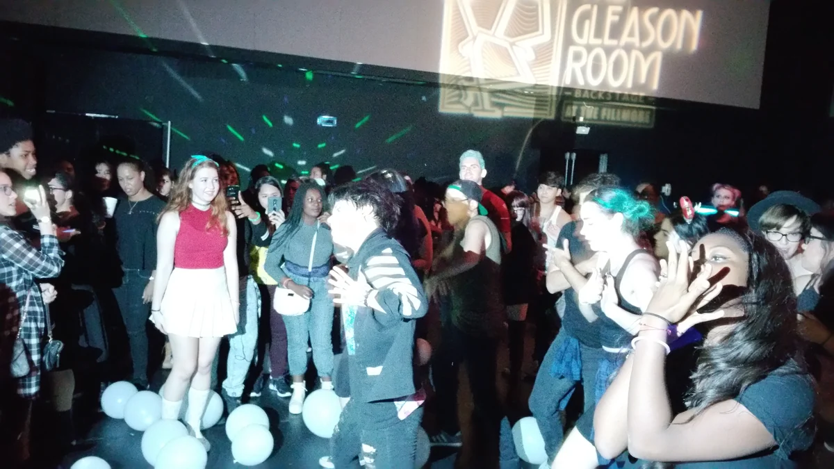 Personas reunidas alrededor de bailarines en una sala de eventos con luces verdes