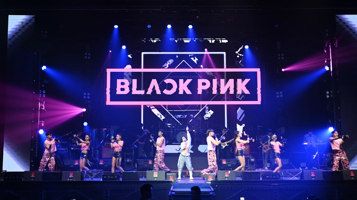 Escenario iluminado en azul y rosa con bailarines ante un gran letrero de BLACKPINK