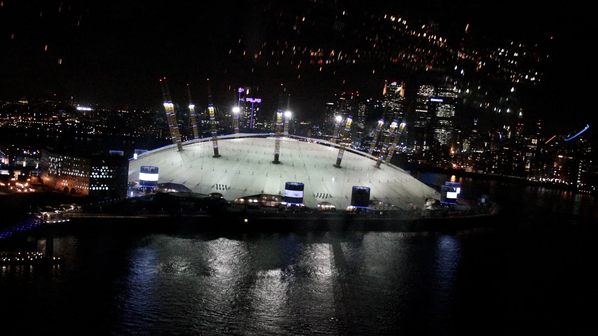Panorama noturno da The O2 iluminada junto ao rio e ao horizonte de Londres