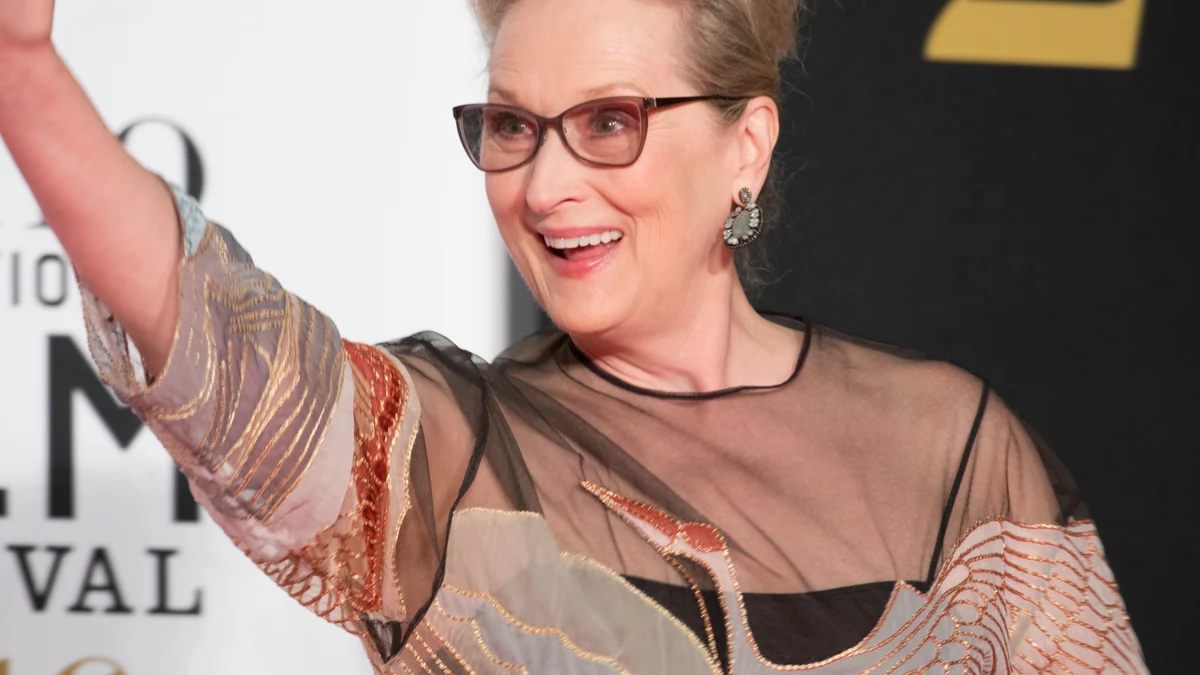 Meryl Streep smiles and raises one arm at a film event