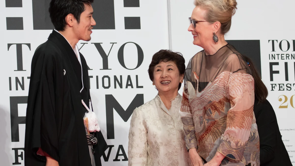 Meryl Streep talks and smiles with two people in front of the Tokyo International Film Festival backdrop