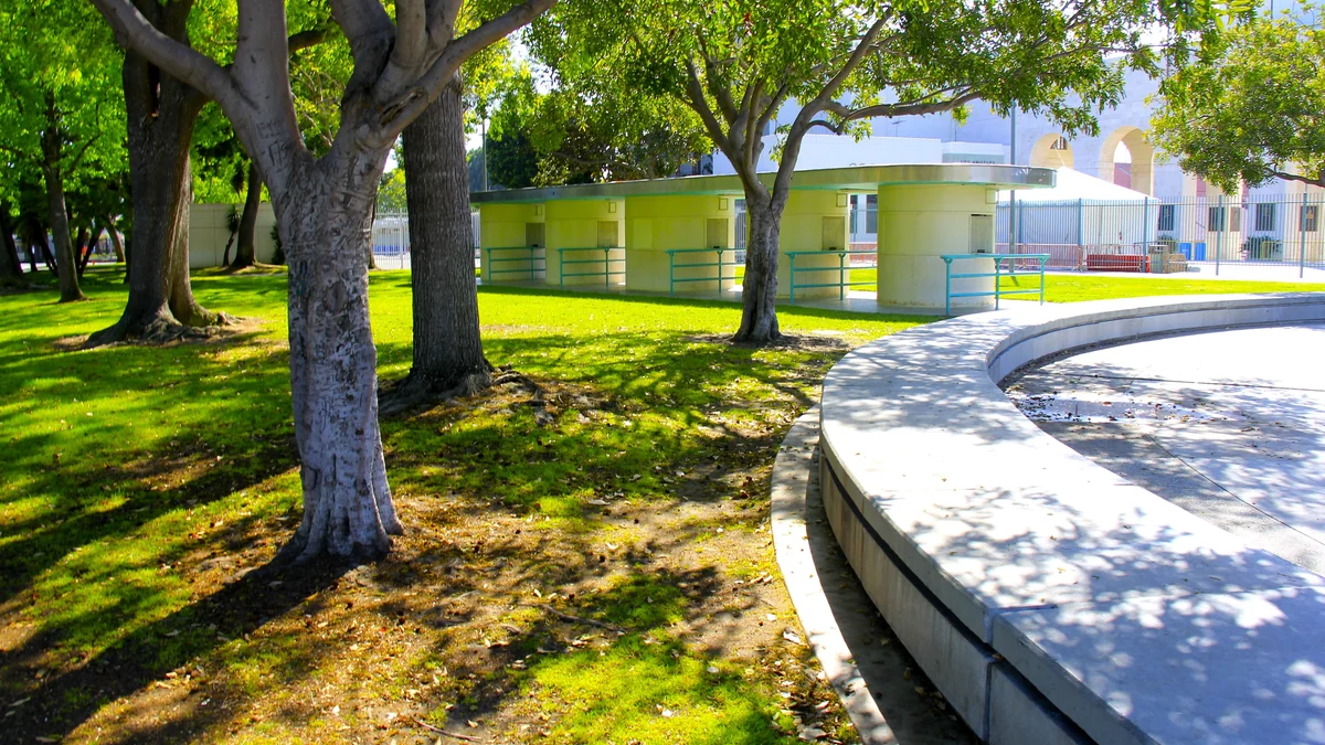 Tree-lined lawn with a low building and curved bench near the Los Angeles Memorial Coliseum