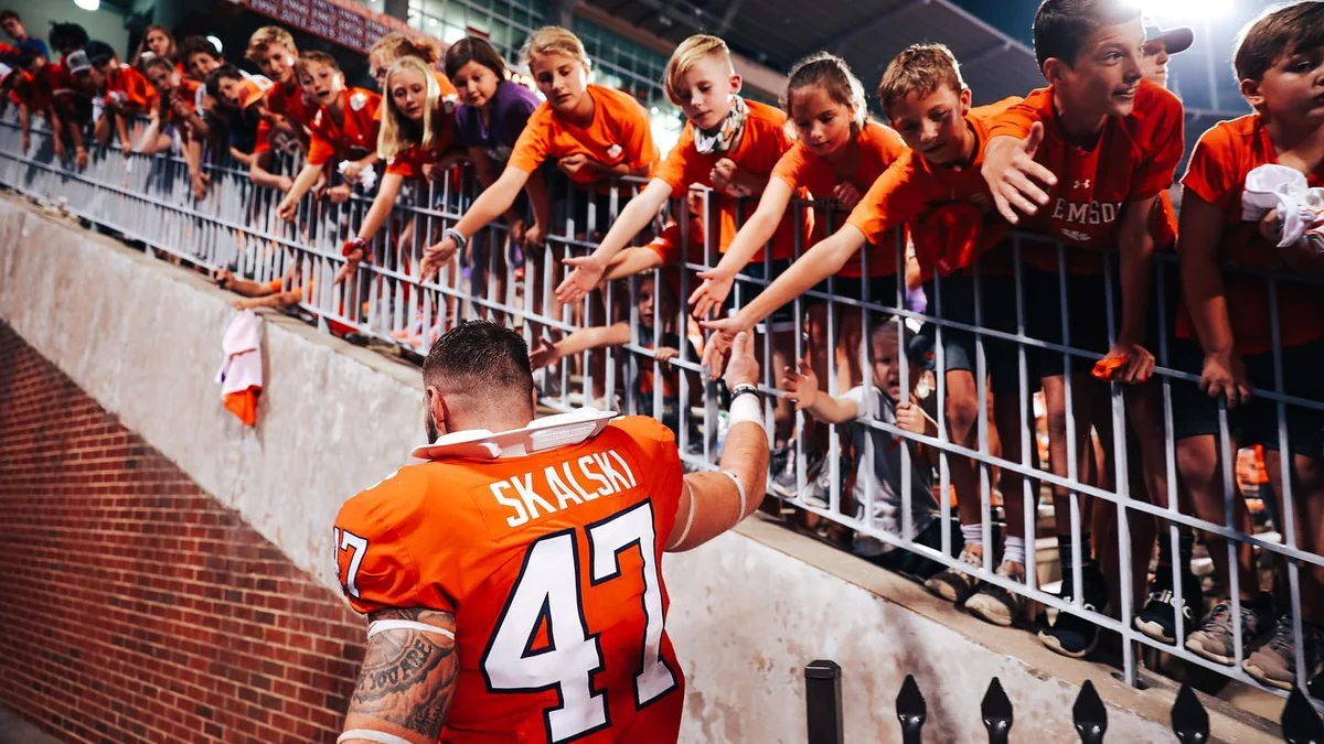 Clemson player wearing number 47 greets children leaning over a stadium railing