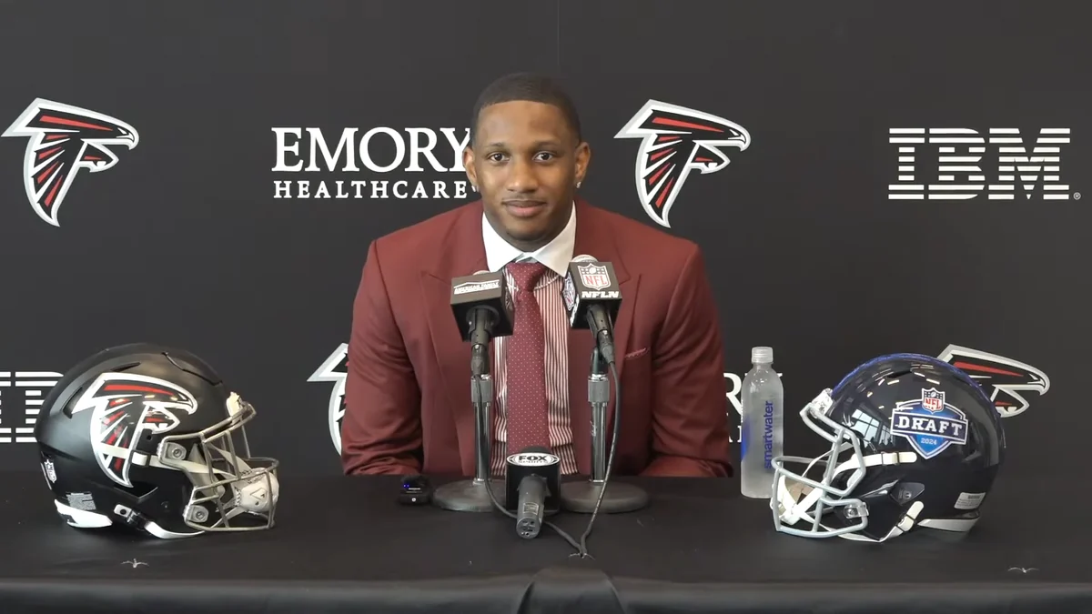 Michael Penix Jr. assis devant des micros lors d’une conférence de presse des Atlanta Falcons, avec deux casques sur la table