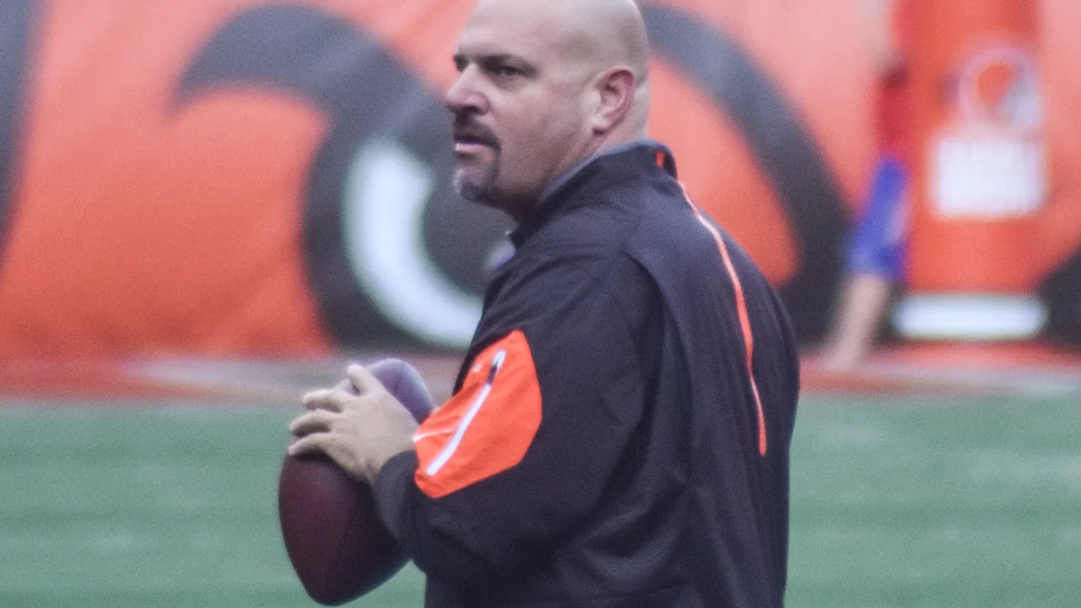 Mike Pettine sostiene un balón de fútbol americano junto a la banda de un campo