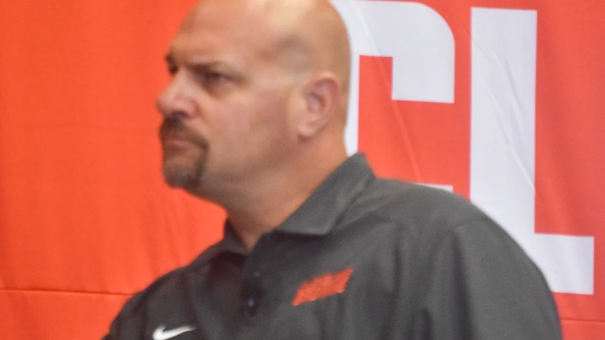Mike Pettine de perfil con un polo oscuro ante un fondo naranja