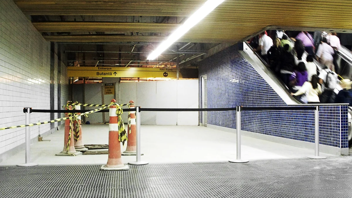 Station area under construction with cones, caution tape, a busy escalator, and a sign for Butantã.