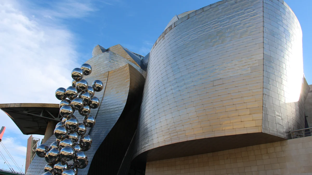 Fachada curva revestida de metal do Museu Guggenheim Bilbao ao lado de uma escultura formada por esferas refletoras