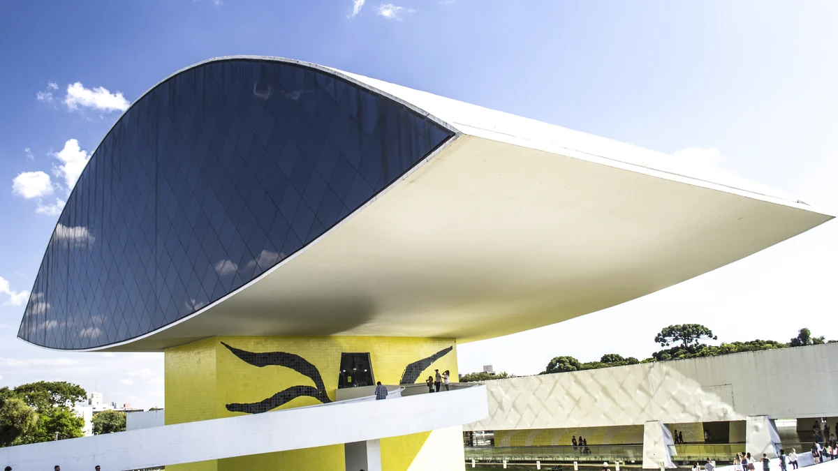 Fachada curva e escura do Museu Oscar Niemeyer acima da base amarela e de uma rampa branca