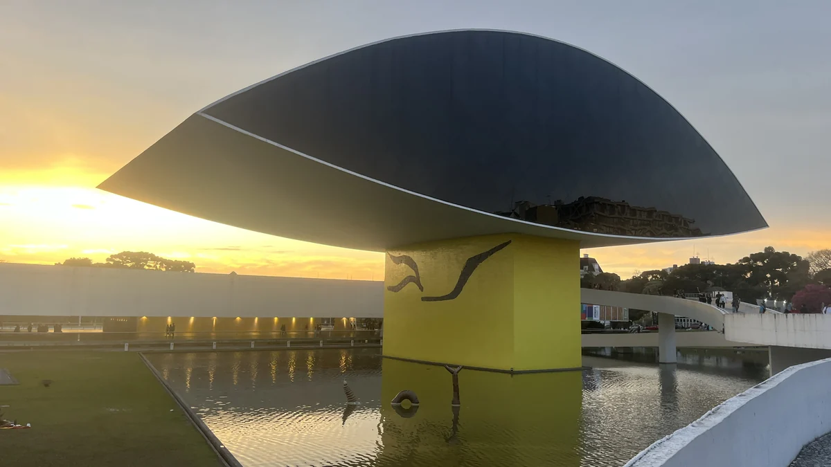 Museu Oscar Niemeyer ao entardecer, com o edifício escuro refletido na água