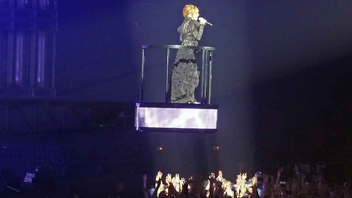 Mylène Farmer sings on an elevated platform above the audience under blue light