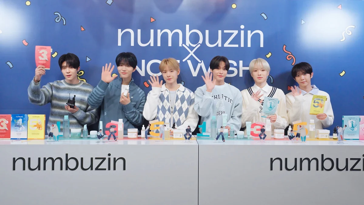 Los seis integrantes de NCT WISH saludan detrás de un mostrador con cosméticos y figuras decorativas.