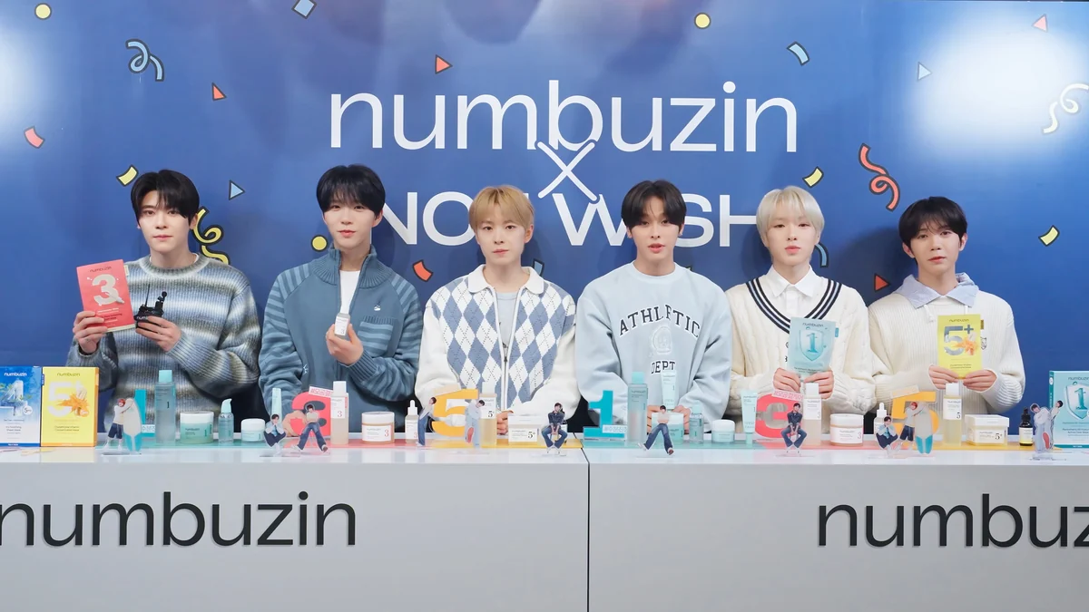 Los seis integrantes de NCT WISH están de pie detrás de un mostrador con envases coloridos de cosméticos, ante un panel azul.