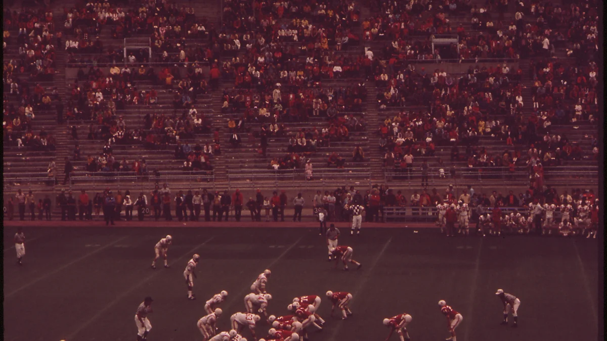 Wide view of a historic Nebraska football game with players on the field and stands in the background
