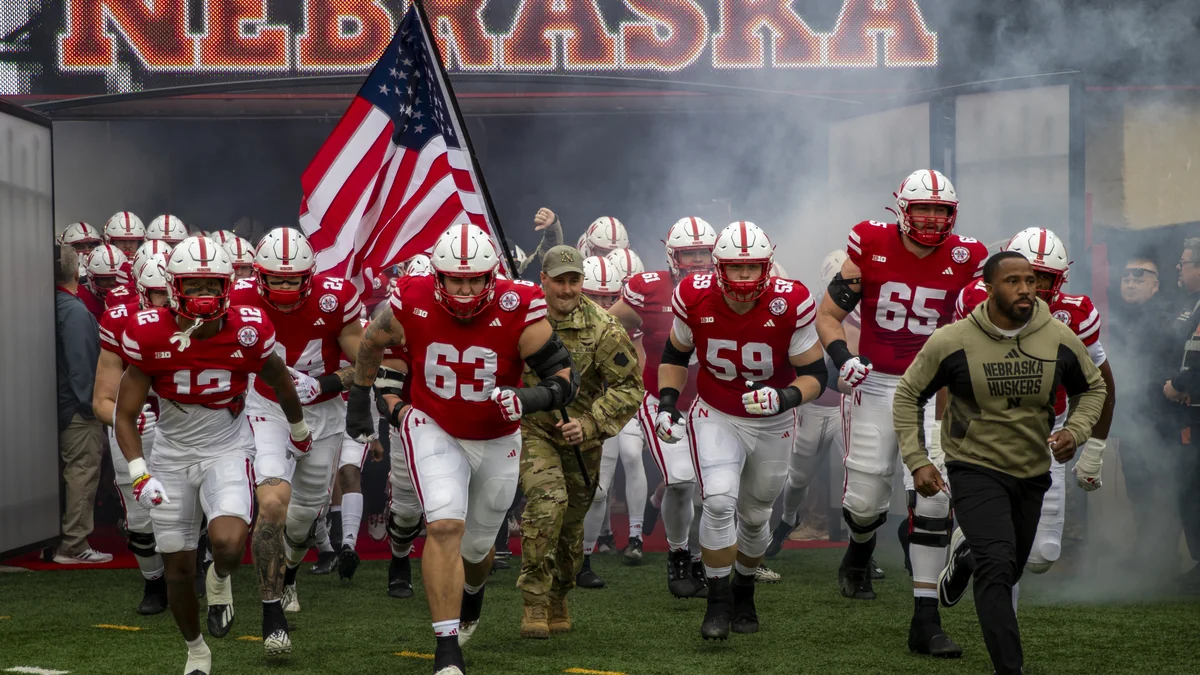 Nebraska players run onto the field through smoke alongside a United States flag