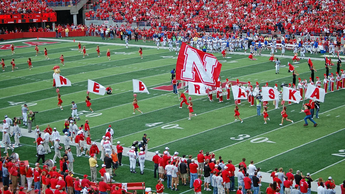 An N flag and banners spelling Nebraska are carried across the field before crowded stands