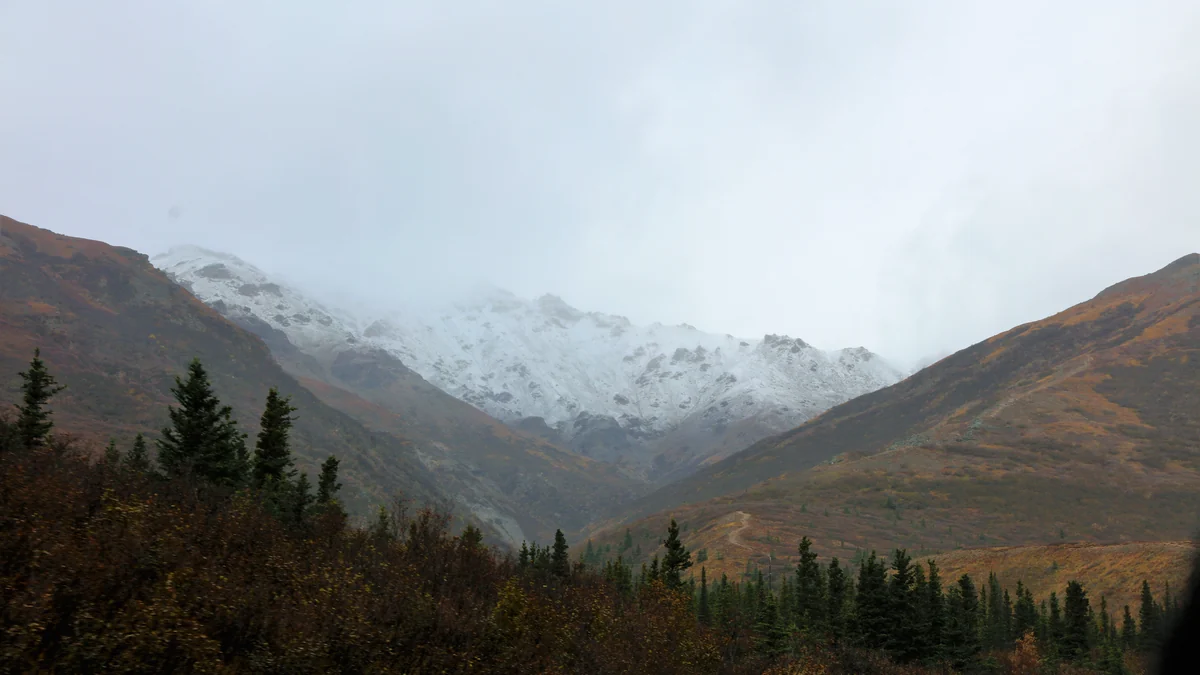 Mountains with fresh snow between autumn slopes and dark conifers