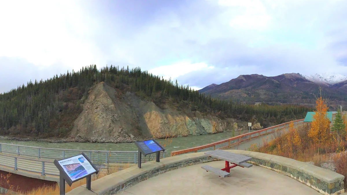 Overlook with panels, a bench and walkway facing a river, hills and mountains