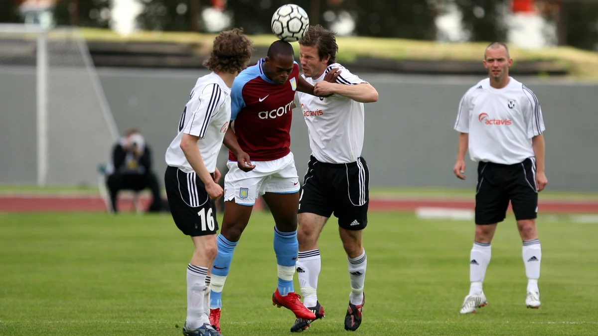 Jogador do Aston Villa disputa uma bola pelo alto com atletas de uniforme branco