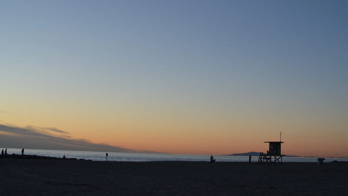 Plage au crépuscule avec un poste de sauveteurs en silhouette et des personnes près de l’eau
