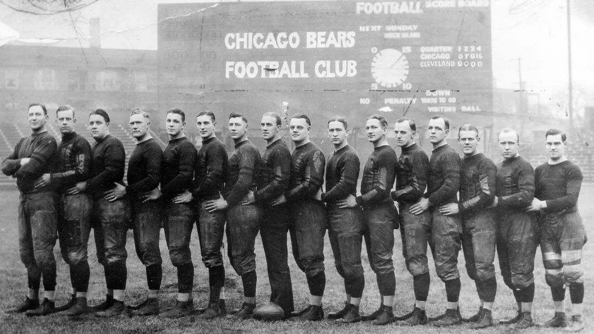Equipe do Chicago Bears de 1924 posa em fila no campo diante de um placar